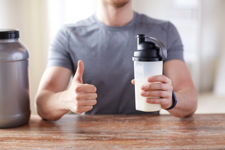 sport, fitness, healthy lifestyle and people concept - close up of man in fitness bracelet with protein shake bottle showing thumbs upの写真素材