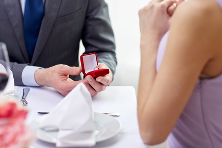 couple, love, engagement and holiday concept - close up of excited young woman and boyfriend giving her ring at restaurantの写真素材
