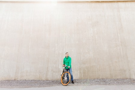 people, style, leisure and lifestyle - happy young hipster man with fixed gear bike on city street