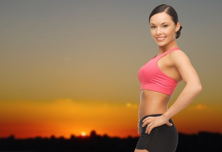 people, fitness and sport concept - happy asian woman posing outdoors over sunset skyline backgroundの写真素材