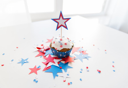 independence day, celebration, patriotism and holidays concept - close up of glazed cupcake or muffin decorated with star and cofetti on table at 4th july partyの写真素材