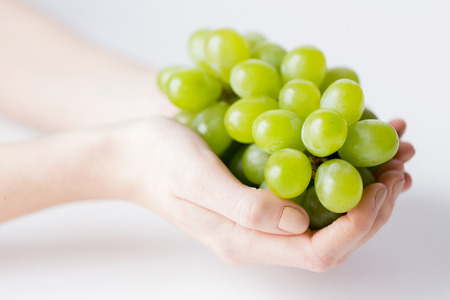 healthy eating, dieting, vegetarian food and people concept - close up of woman hands holding green grape bunch at homeの写真素材