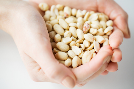 healthy eating, dieting, vegetarian food and people concept - close up of woman hands holding peeled peanuts at homeの写真素材