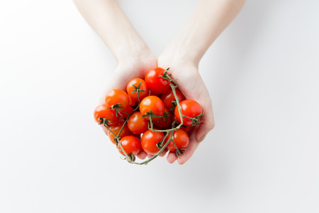 healthy eating, dieting, vegetarian food and people concept - close up of woman hands holding cherry tomatoes bunch at homeの写真素材