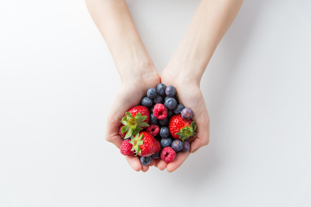 healthy eating, dieting, vegetarian food and people concept - close up of woman hands holding berries at homeの写真素材