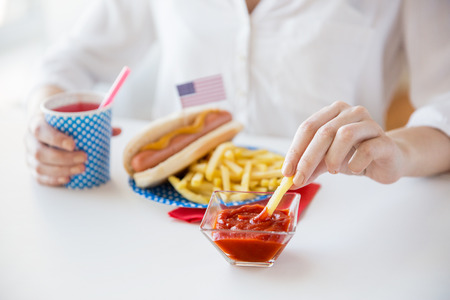 national holidays, celebration, food and patriotism concept - close up of woman eating french fries with hot dog and drinking juice from paper cup at 4th july at party on american independence dayの写真素材