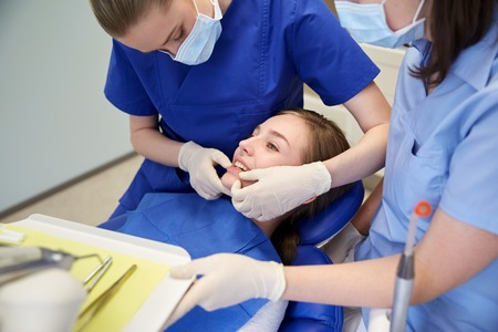 people, medicine, stomatology and teeth care concept - happy female dentist with assistant checking patient girl dental occlusion teeth at dental clinic officeの写真素材