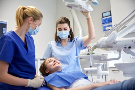 people, medicine, stomatology and health care concept - happy female dentist with assistant and patient girl at dental clinic officeの写真素材