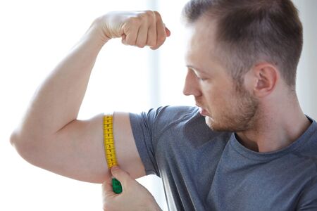 sport, fitness, lifestyle, bodybuilding and people concept - close up of male hands with tape measuring bicepの写真素材