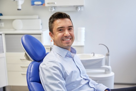 people, medicine, stomatology and health care concept - happy male patient sitting on dental chair at clinic officeの写真素材