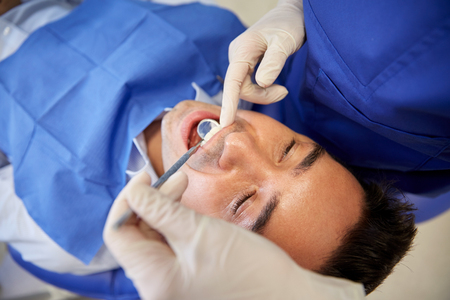 people, medicine, stomatology and health care concept - close up of female dentist with dental mirror checking up male patient teeth at dental clinic officeの写真素材