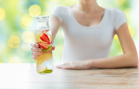 healthy eating, drinks, diet, detox and people concept - close up of woman with fruit water in glass bottle over green lights backgroundの写真素材