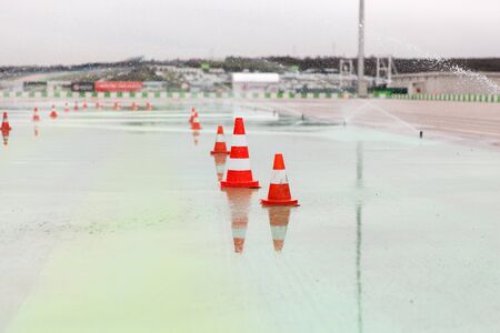 racing, motosports, extreme and motoring concept - traffic cones and sprinklers on wet speedway of stadiumの写真素材