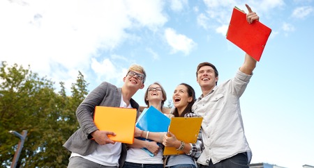 education, friendship, future and teenage concept - group of happy students with folders pointing finger at campus or parkの写真素材