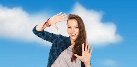 people and teens concept - happy smiling pretty teenage girl showing hands over blue sky and clouds...