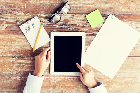 business, education, people and technology concept - close up of female hands pointing finger to tablet pc computer black blank screen with paper, notebook and eyeglassesの写真素材