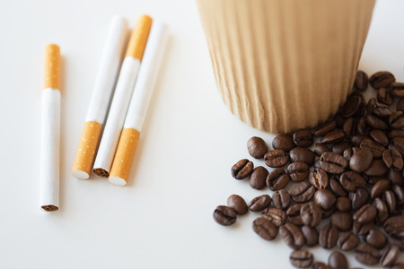 bad habits, addiction and unhealthy lifestyle concept - close up of cigarettes, coffee cup and beans on tableの写真素材