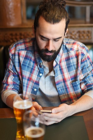 people and technology concept - man with smartphone drinking beer and reading message at barの写真素材