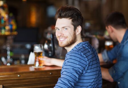 people, leisure and drinks concept - happy young man drinking beer at bar or pubの写真素材