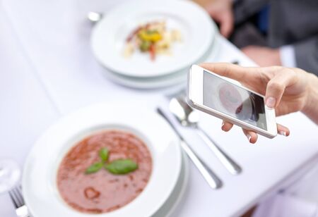 people, leisure, eating and technology concept - close up of couple with smartphones taking picture of food at restaurantの写真素材