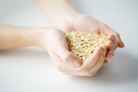healthy eating, dieting, vegetarian food and people concept - close up of woman hands holding oatmeal flakes at homeの写真素材