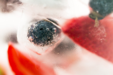 healthy eating, drinks, diet and detox concept - close up of fruit water with strawberry, blackcurrant or blueberry and ice cubes over glassの写真素材