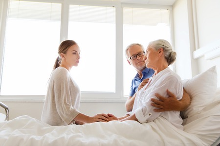 medicine, support, family health care and people concept - senior man and young woman visiting and cheering her ill grandmother at hospital wardの写真素材