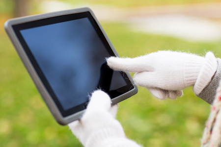 technology, advertisement and people concept - close up of hands in autumn gloves holding tablet pc computer with black blank screen outdoorsの写真素材