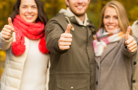 friendship, gesture, season and people concept - close up of happy friends showing thumbs up in autumn parkの写真素材