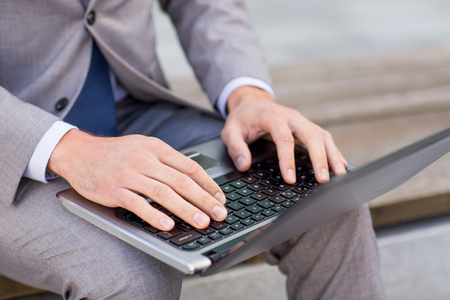 business, technology and people concept - close up of man with laptop computer sitting on bench in cityの写真素材