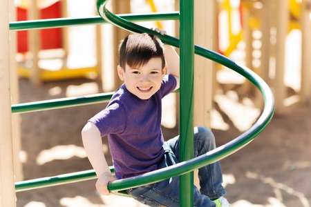 summer, childhood, leisure and people concept - happy little boy on children playground climbing...