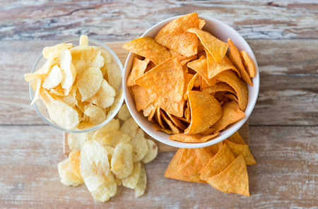 fast food, junk-food, cuisine and eating concept - close up of potato crisps and corn nachos in...