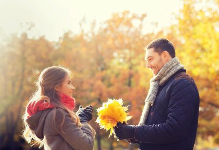 love, relationship, family, season and people concept - smiling couple with bunch of leaves in autumn parkの写真素材