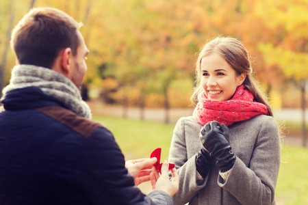 love, family, autumn and people concept - smiling couple with engagement ring in small red gift box outdoorsの写真素材
