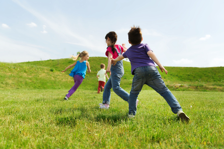 summer, childhood, leisure and people concept - group of happy kids playing tag game and running on green field outdoors summer, childhood, leisure and people concept - group of happy kids playing tag game and running on green field outdoors