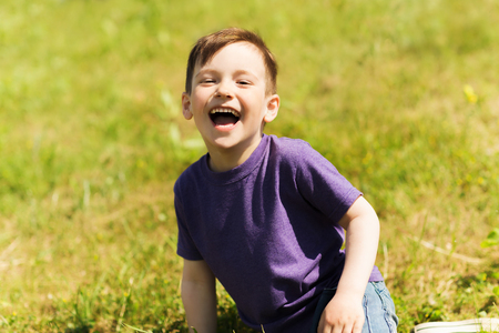 summer, childhood, leisure and people concept - happy little boy sitting on grass and laughing outdoorsの写真素材