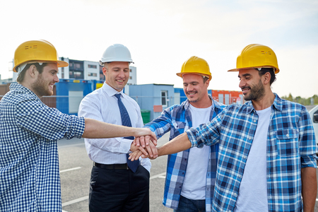 business, building, partnership, gesture and people concept - smiling builders and architects in hardhats with hands on top outdoorsの写真素材
