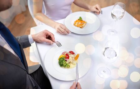 restaurant, food, people, date and holiday concept - close up of couple eating appetizers at restaurant over holidays lights backgroundの写真素材