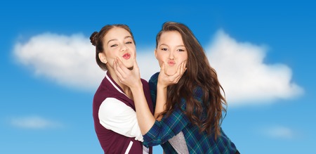 happy smiling pretty teenage girls having fun and making faces over blue sky and clouds backgroundの写真素材