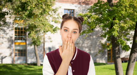 people, school, education, expression and teens concept - confused teenage student girl covering her mouth by hand over summer campus backgroundの写真素材