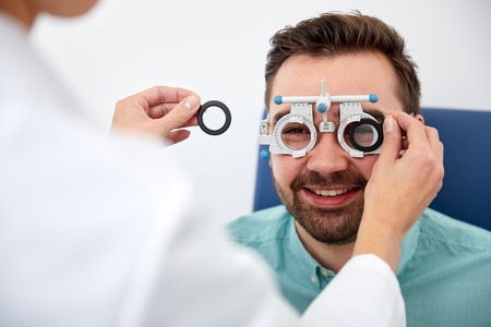 health care, medicine, people, eyesight and technology concept - optometrist with trial frame checking patient vision at eye clinic or optics storeの写真素材
