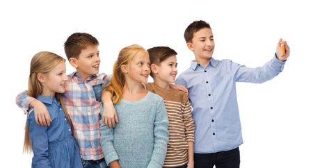 childhood, friendship, technology and people concept - happy children talking selfie by smartphoneの写真素材