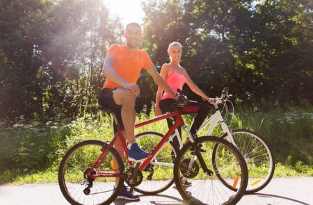 fitness, sport, people and healthy lifestyle concept - happy couple riding bicycle outdoors at summerの写真素材