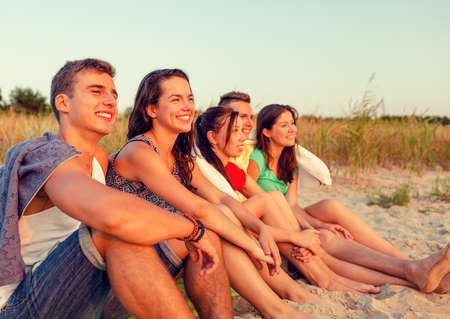 friendship, happiness, summer vacation, holidays and people concept - group of smiling friends sitting beachの写真素材