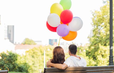 love, holidays, summer, dating and people concept - happy couple with air balloons in city sitting on benchの写真素材