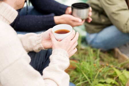 adventure, travel, tourism and people concept - close up of hikers drinking tea from cups at campの写真素材