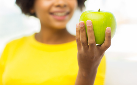 people, food, healthy eating and dental care concept - close up of happy african american young woman with green apple at homeの写真素材