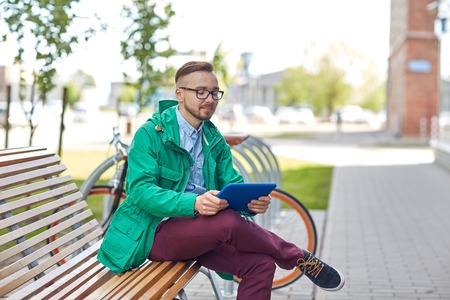 people, style, technology and lifestyle - happy young hipster man with tablet pc computer and fixie bike sitting on bench in cityの写真素材
