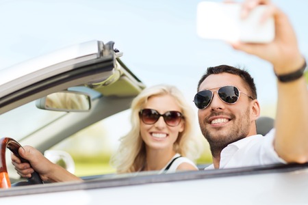 road trip, leisure, couple, technology and people concept - happy man and woman driving in cabriolet...