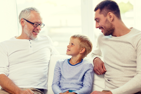 family, happiness, generation and people concept - smiling father, son and grandfather sitting on couch at homeの写真素材